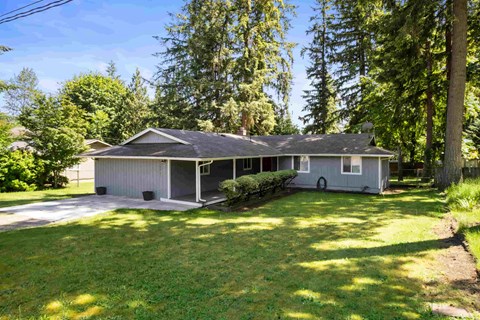 A house with a grey roof and a grey garage door is surrounded by trees.