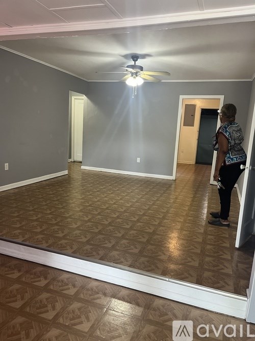 A woman is standing in a room with a ceiling fan and patterned flooring.