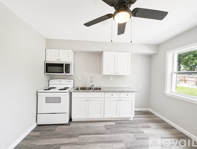 A kitchen with white appliances and cabinets, a ceiling fan, and a window.
