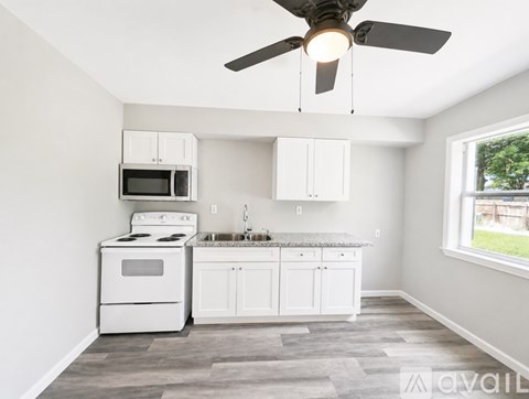 A kitchen with white appliances and cabinets, a ceiling fan, and a window.