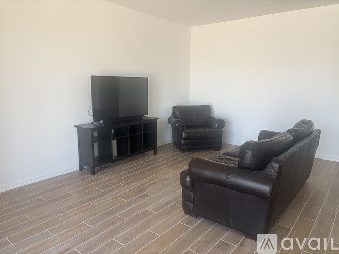 A black leather sofa, chair and TV stand in a room with wooden flooring.
