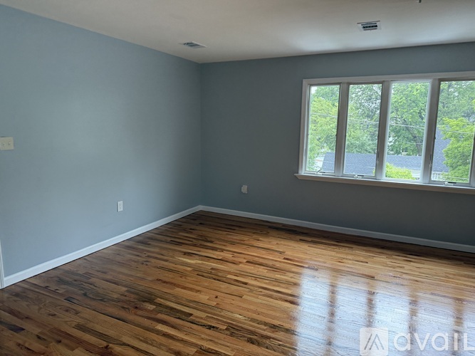 A room with wooden flooring and a window showing trees outside.