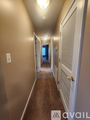 A hallway with a white door on the right and a window in the distance.