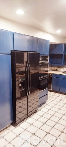 A kitchen with blue cabinets and a black fridge.