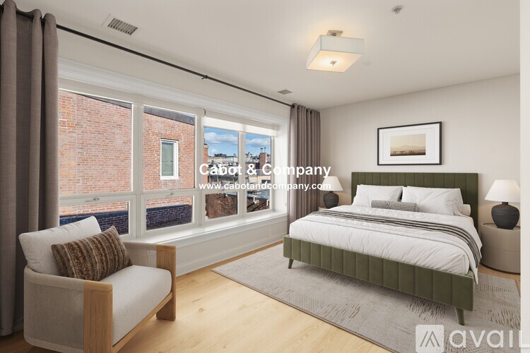 A bedroom with a large bed, a chair, and a window overlooking a brick building.