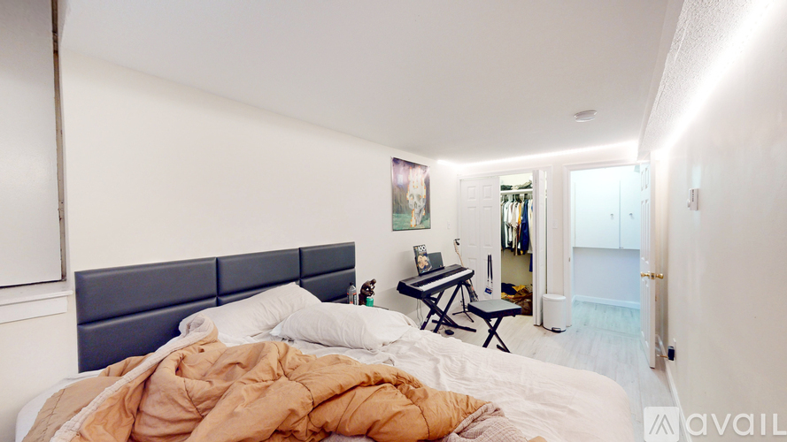 A bedroom with a bed covered in a blanket and a desk with a chair in the background.