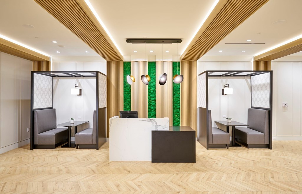 A room with a white reception desk and two grey booths.