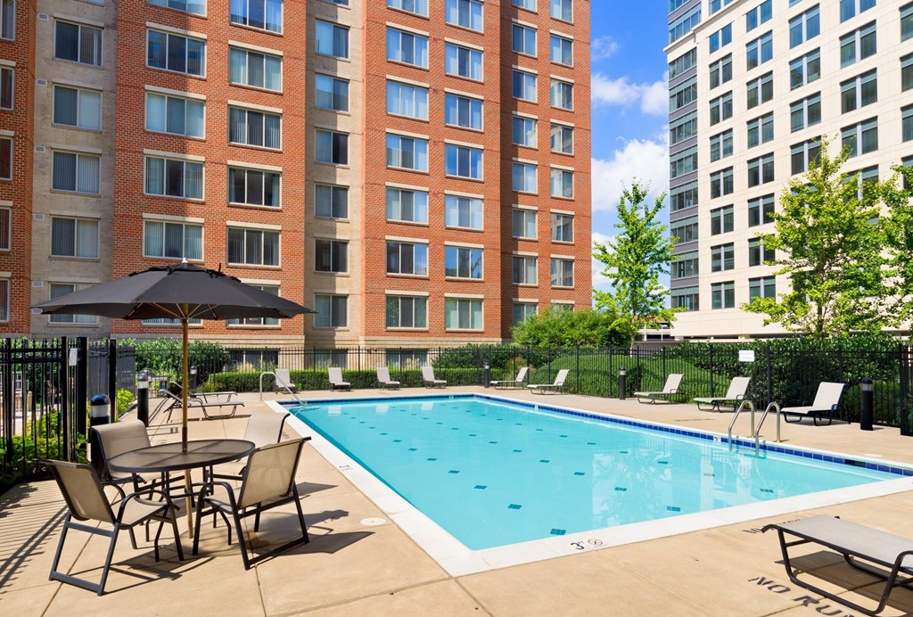 A pool surrounded by chairs and umbrellas in front of a brick building.