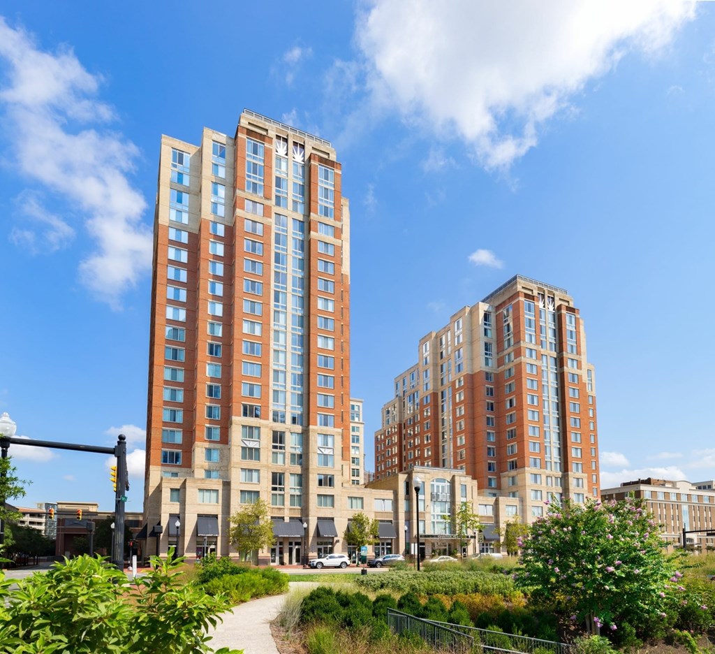 Two tall buildings with many windows are surrounded by greenery.