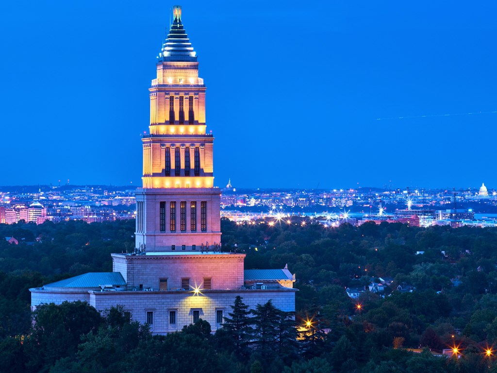 A tall white tower with a pointed top is lit up at night.
