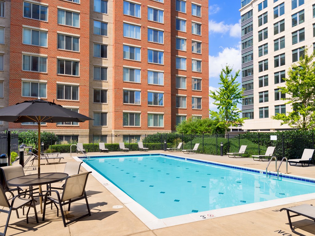 A pool surrounded by chairs and umbrellas in front of a red brick building.