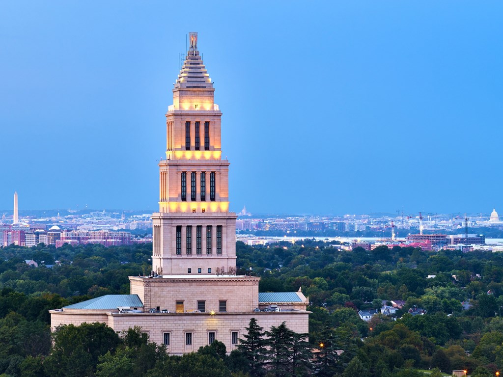 A large white building with a tall spire is lit up at dusk.