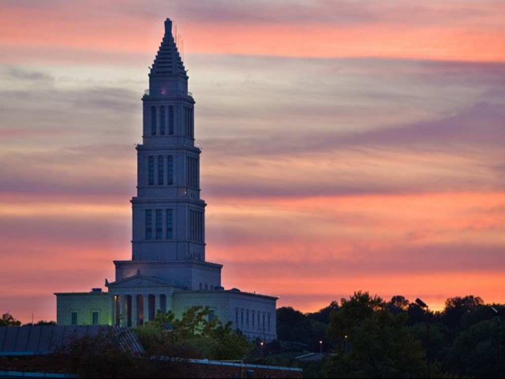 A large white building with a tower is lit up at dusk.