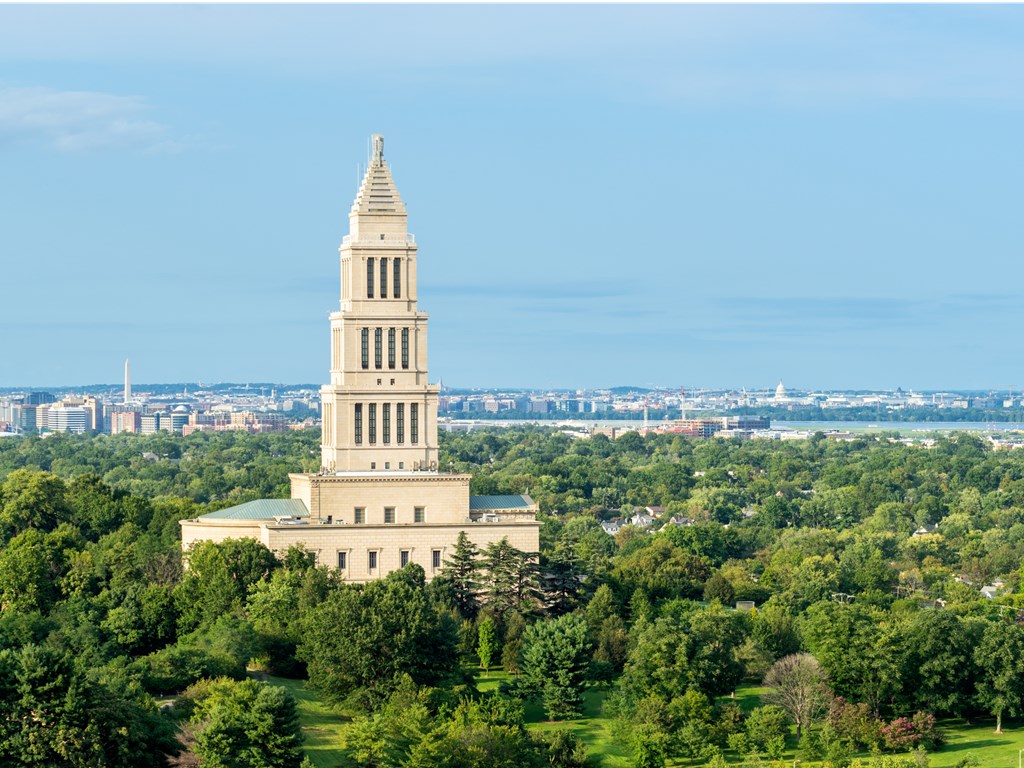 A large white building with a spire is surrounded by trees.