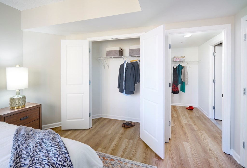 A bedroom with a bed, a nightstand with a lamp, and a closet with clothes.