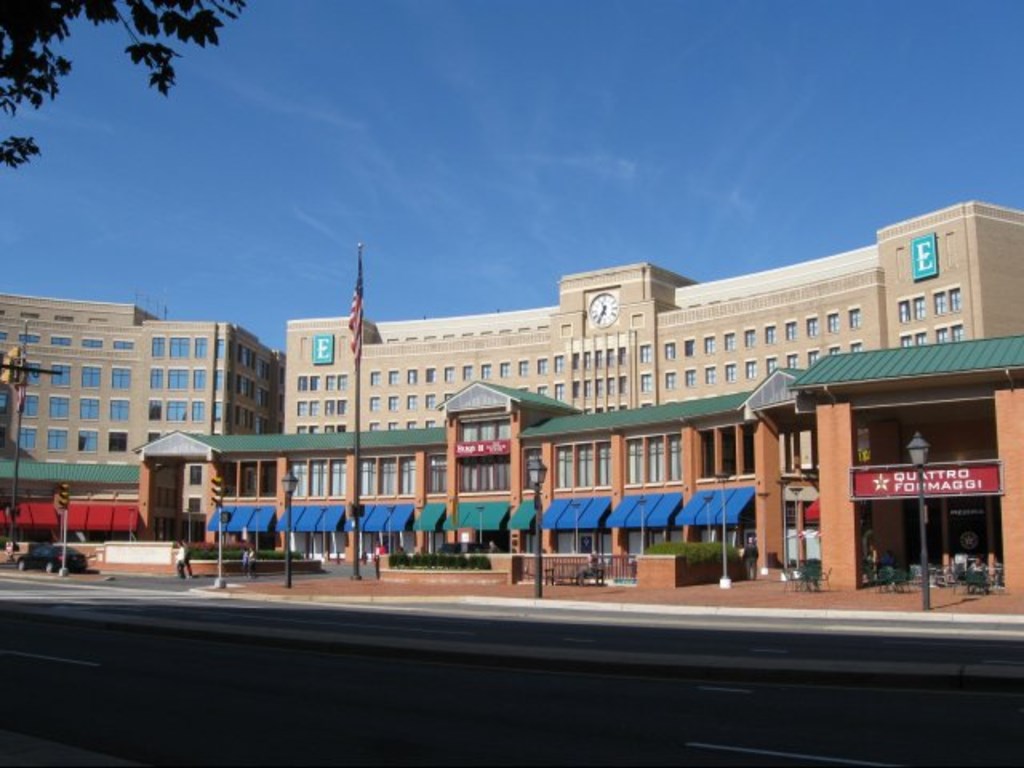 A large building with a clock tower is surrounded by other buildings and has a Subway restaurant in front.