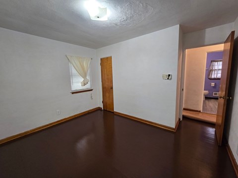 A room with a brown floor and a white wall with a window and a door.