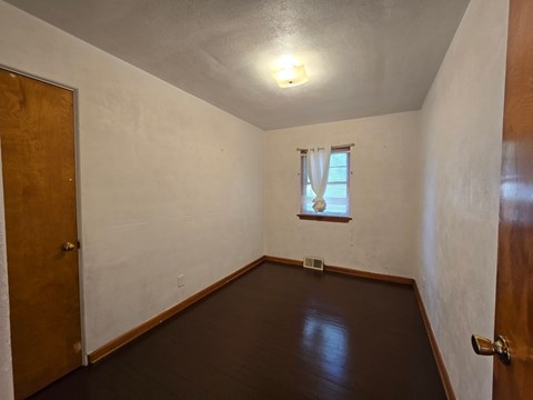 A room with a brown floor and a window with white curtains.