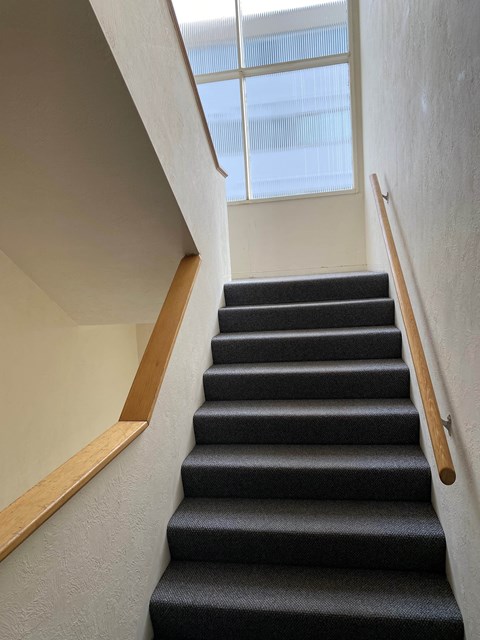 A staircase with a wooden handrail and black steps.
