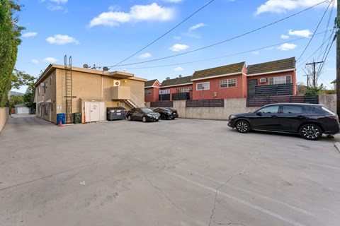 A black car is parked in a lot with other cars and buildings in the background.