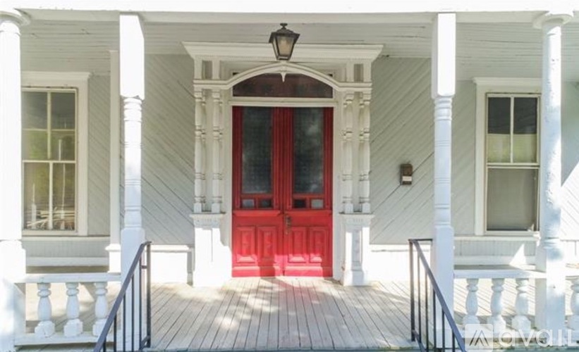 A white house with a red door and a black railing.
