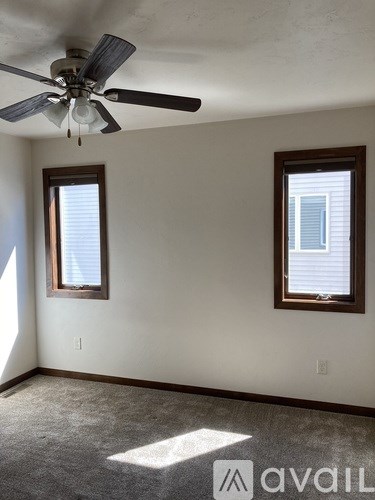 A room with a ceiling fan and two windows.