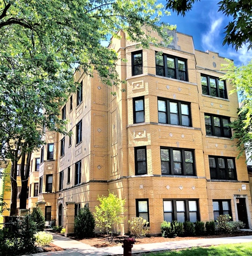 A large, beige, multi-story building with many windows and a tree in front.