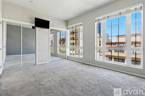 A spacious living room with a grey carpet and large windows overlooking a cityscape.