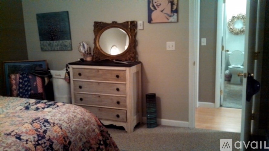 A wooden dresser with a mirror on top is in a room with a bed and a doorway leading to a bathroom.