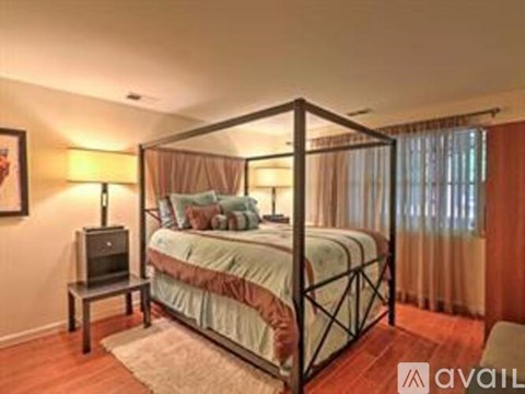 A bedroom with a four-poster bed and a small table with a lamp.