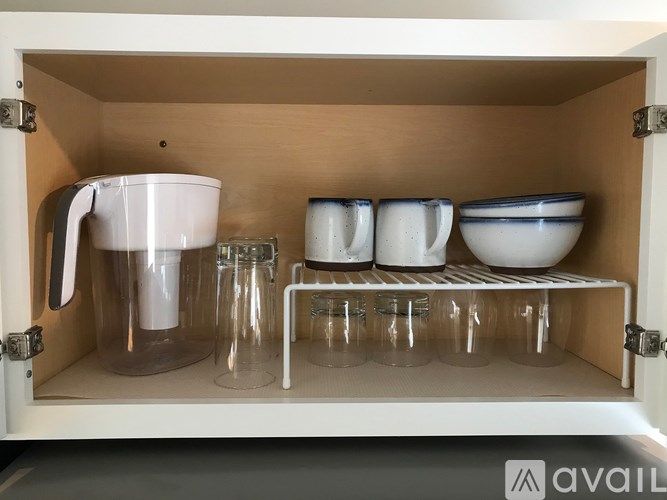 A kitchen cabinet with a mixer, bowls, and glasses.