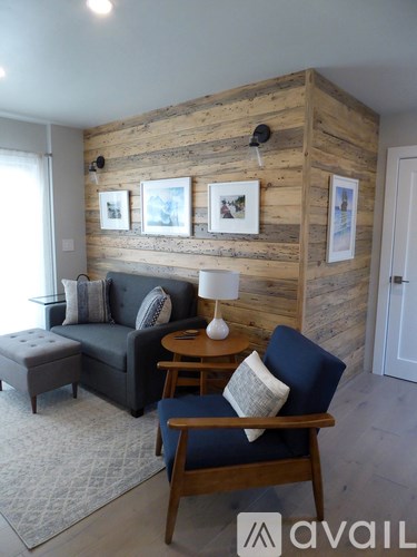 A living room with a blue couch, a wooden chair, and a wooden wall.