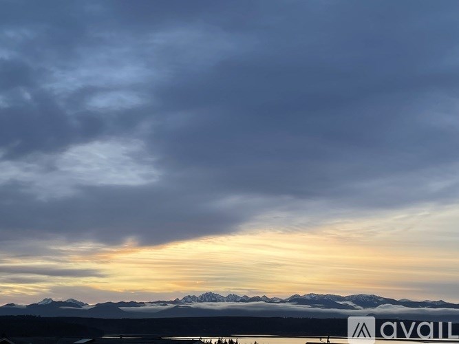 A cloudy sky with mountains in the distance and a body of water in the foreground.