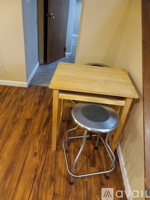 A wooden stool with a metal base is in a room with wooden flooring.
