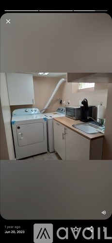 A white washing machine is in a kitchen with a sink and a window.