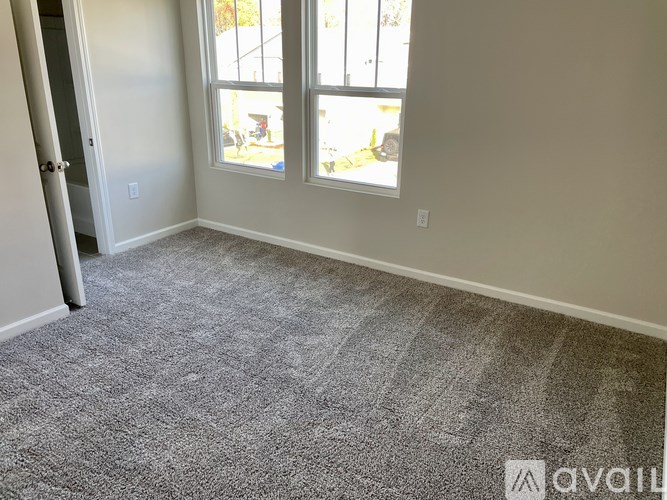 A room with a grey carpet and a window.