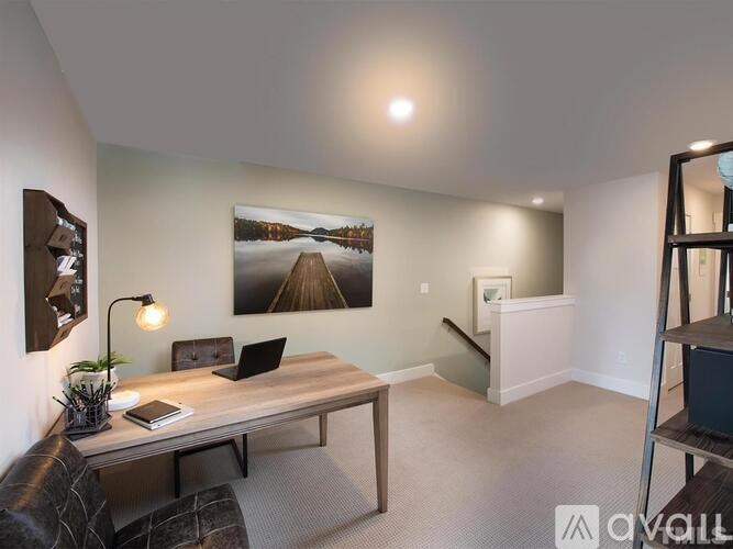 A room with a wooden table, a laptop, a lamp, a plant, and a painting on the wall.