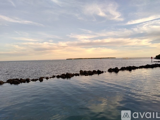 A calm body of water with a rocky shore and a cloudy sky.