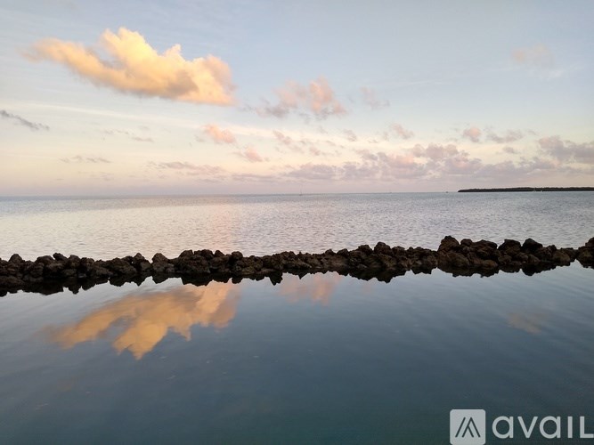 A serene seascape with a line of rocks in the foreground and a cloudy sky above.