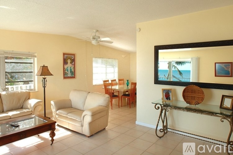 A living room with a white couch, a glass table, and a mirror on the wall.