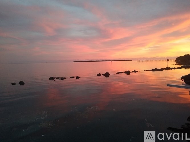 A serene sunset view with a pier and rocks in the foreground.