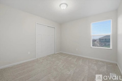 A bedroom with a carpeted floor, a window with blinds, and a door.