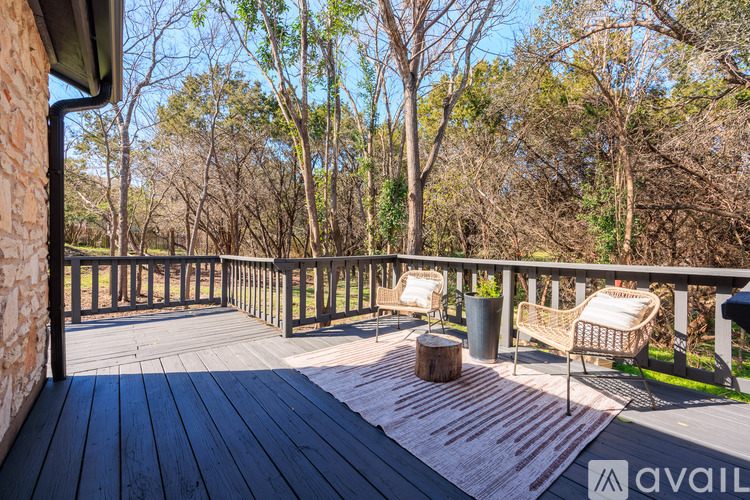 A wooden deck with a wicker chair and a table is surrounded by trees.