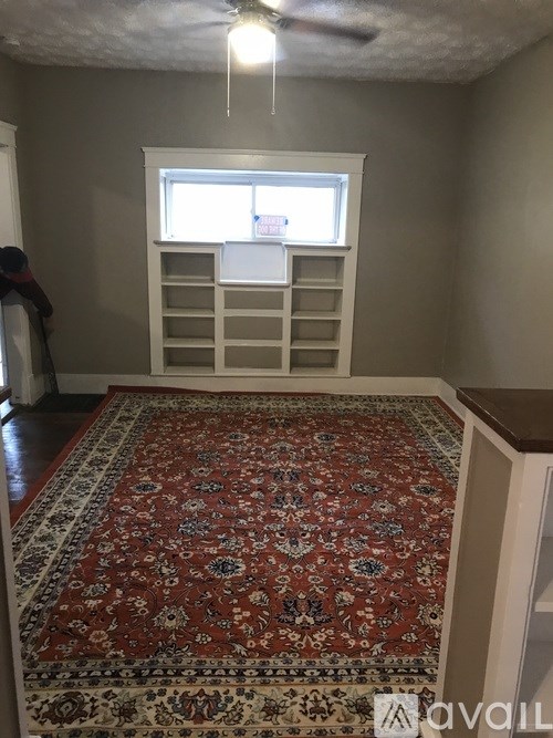 A room with a rug on the floor and a window with blinds.