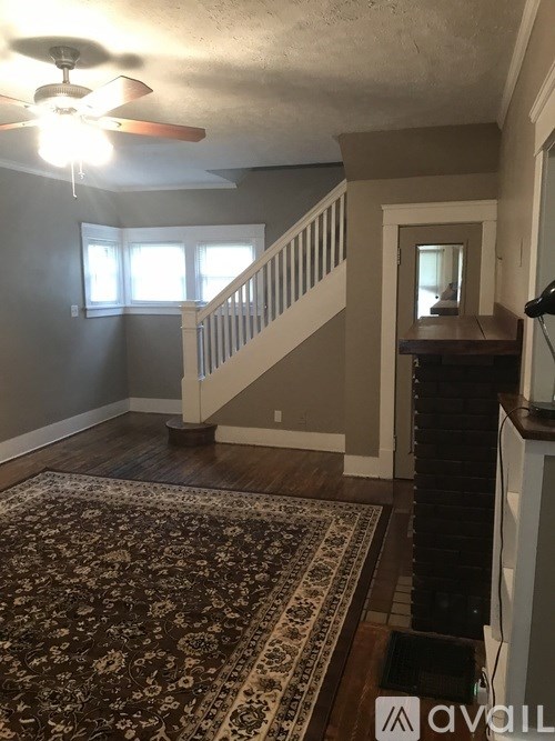 A living room with a rug, a ceiling fan, and a staircase.