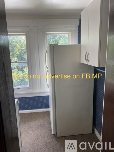 A white refrigerator in a kitchen with a window and curtains.