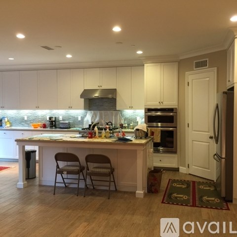 A kitchen with white cabinets and a wooden island with two chairs.