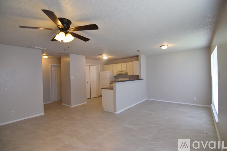 A spacious room with a ceiling fan and a kitchenette in the background.