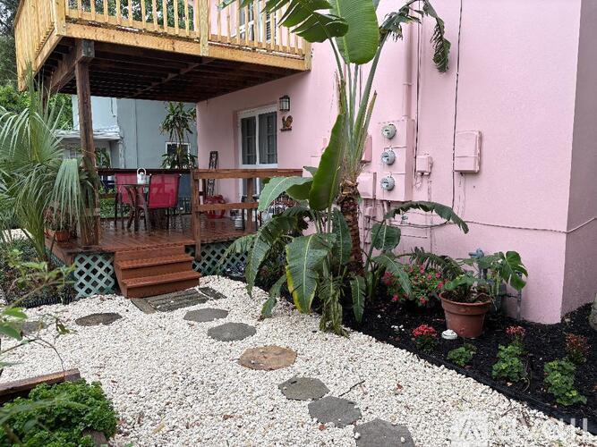 A pink house with a wooden balcony and a garden in front.