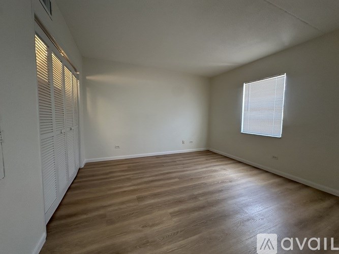 A spacious room with wooden flooring and a window on the right wall.